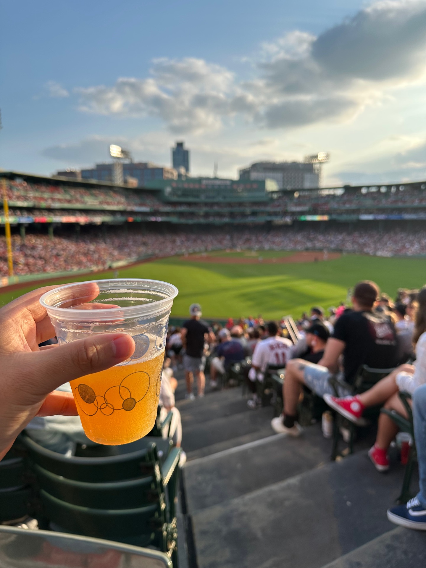 A hand holding a beer at Fenway Park during a baseball game